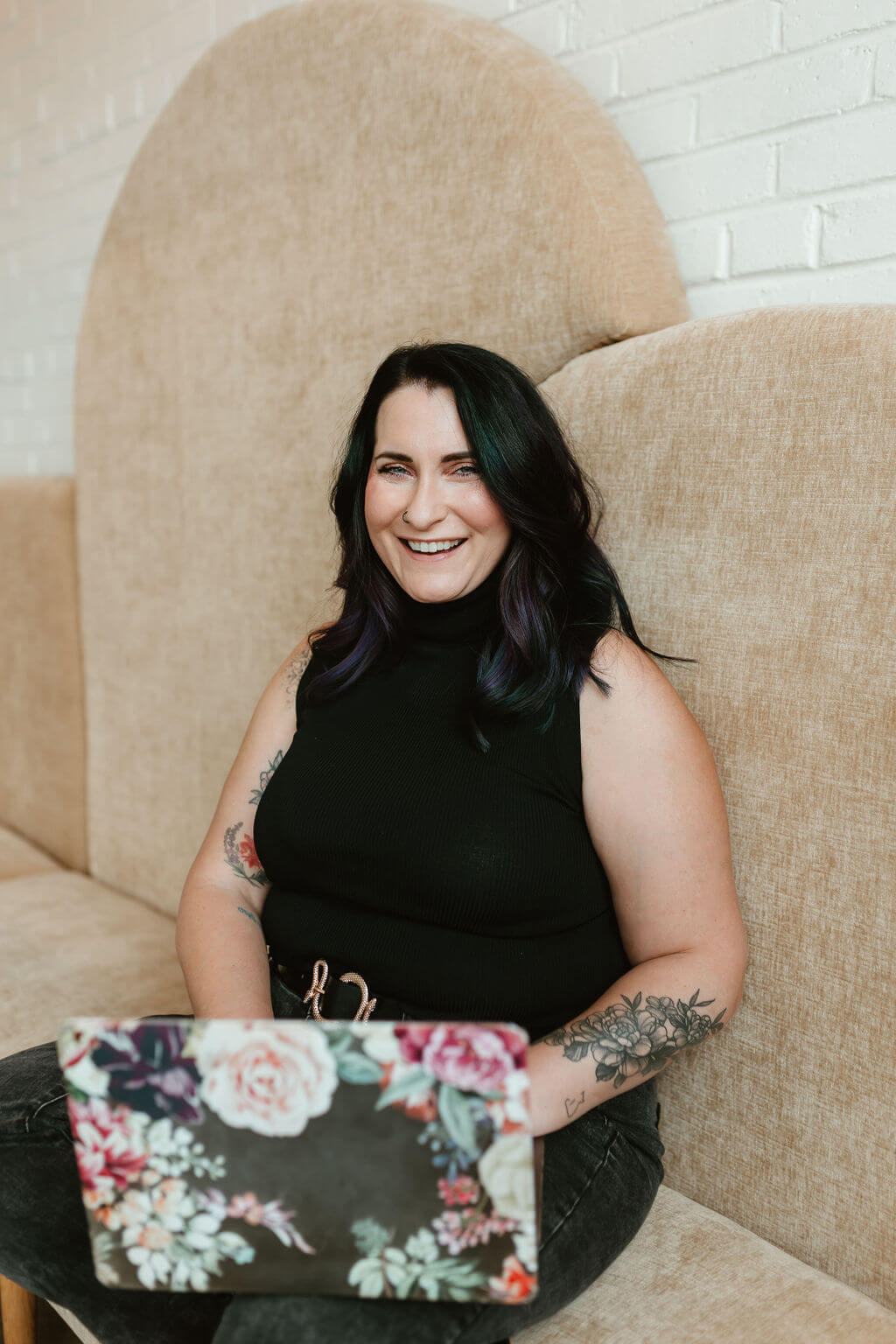 Smiling conference event planner working on a floral-covered laptop, seated in a modern lounge space—confident, approachable, and ready to lead high-impact events.