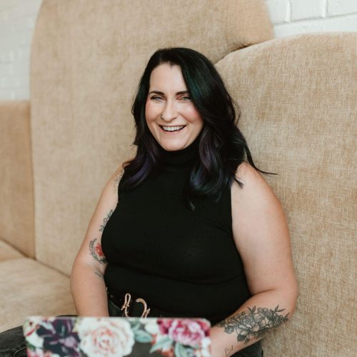 Smiling conference event planner working on a floral-covered laptop, seated in a modern lounge space—confident, approachable, and ready to lead high-impact events.